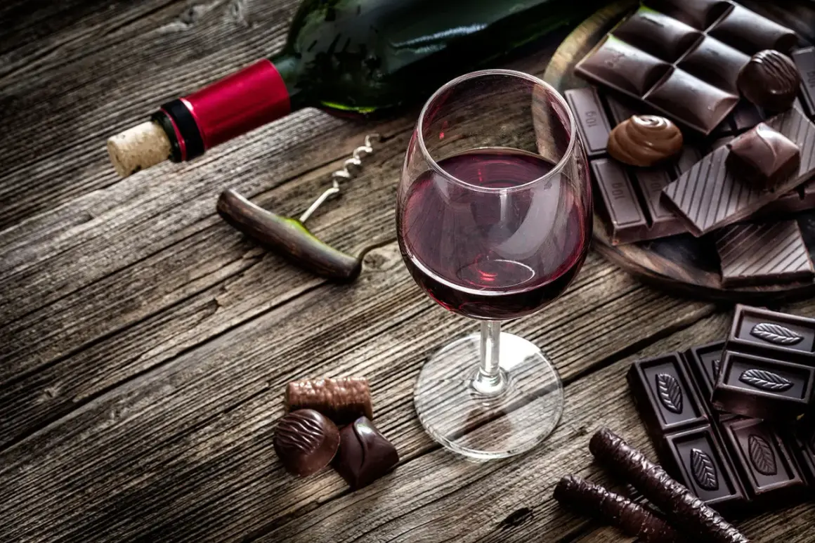 Ein Glas Rotwein und verschiedene Schokoladenstücke auf Holztisch. Ein Korkenzieher liegt daneben.