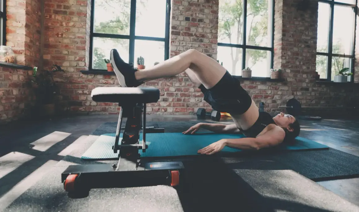 Femme effectuant un hip thrust sur un banc dans une salle de sport au style industriel.