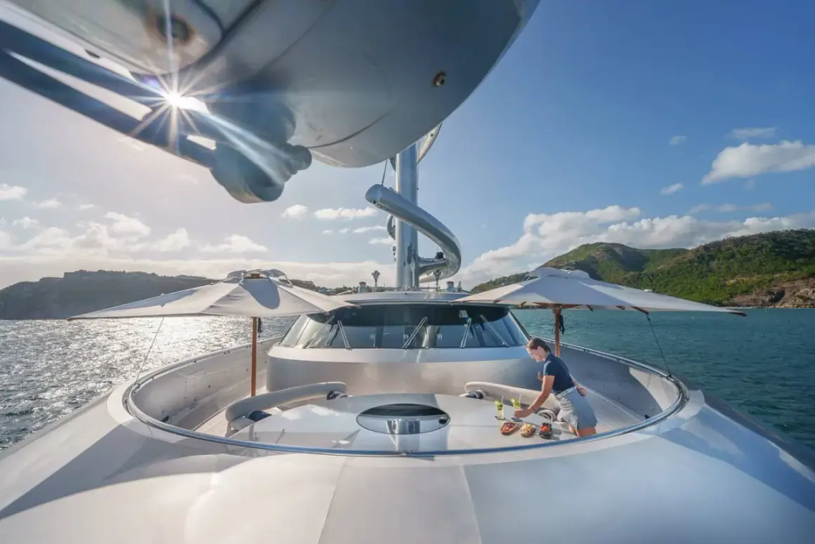 Un membro dell'equipaggio prepara un rinfresco sul ponte del Maltese Falcon yacht, con il sole che splende sull'acqua cristallina.
