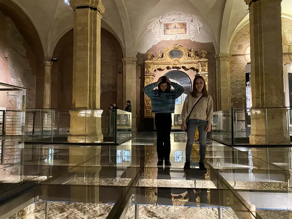 Due ragazze esplorano il Palazzo Madama, con un pavimento in vetro che rivela antiche rovine sottostanti.