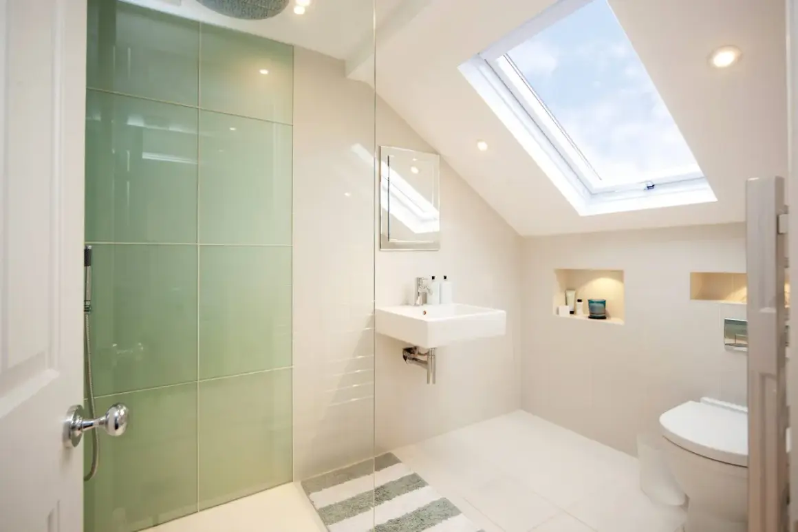 Moderno baño con ducha de cristal verde, lavabo flotante y tragaluz. Ideas para como decorar un baño con estilo y luz natural.