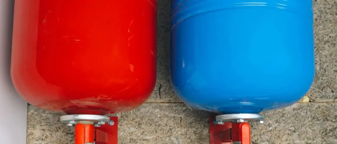 Deux réservoirs, un rouge et un bleu, sont fixés à un mur. Ce sont des éléments essentiels d'un système de chauffage, fonctionnant comme un vase d'expansion.
