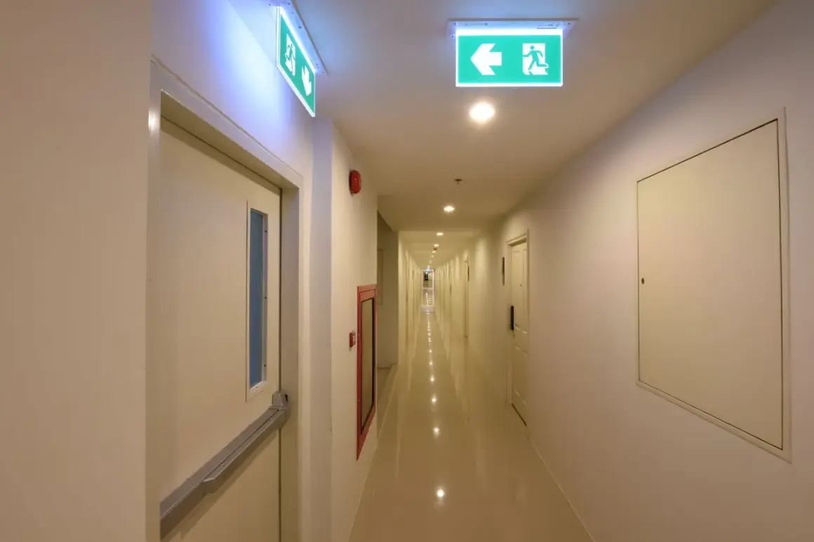 Korytarz hotelowy z zielonymi znakami ewakuacyjnymi, zgodnie z normą PN-EN 1838.