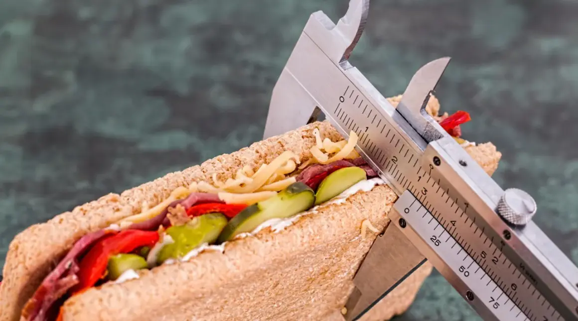 Messung eines Sandwiches mit einem Messschieber, um die Kalorienaufnahme zu kontrollieren. Vielleicht 1500 Kalorien am Tag?