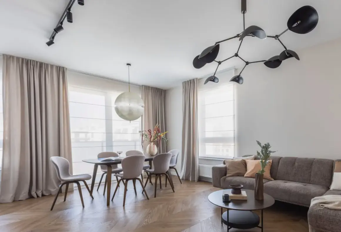 Nowoczesne oświetlenie salonu z jadalnią: designerska lampa nad stołem i reflektory na suficie tworzą przytulną atmosferę.
