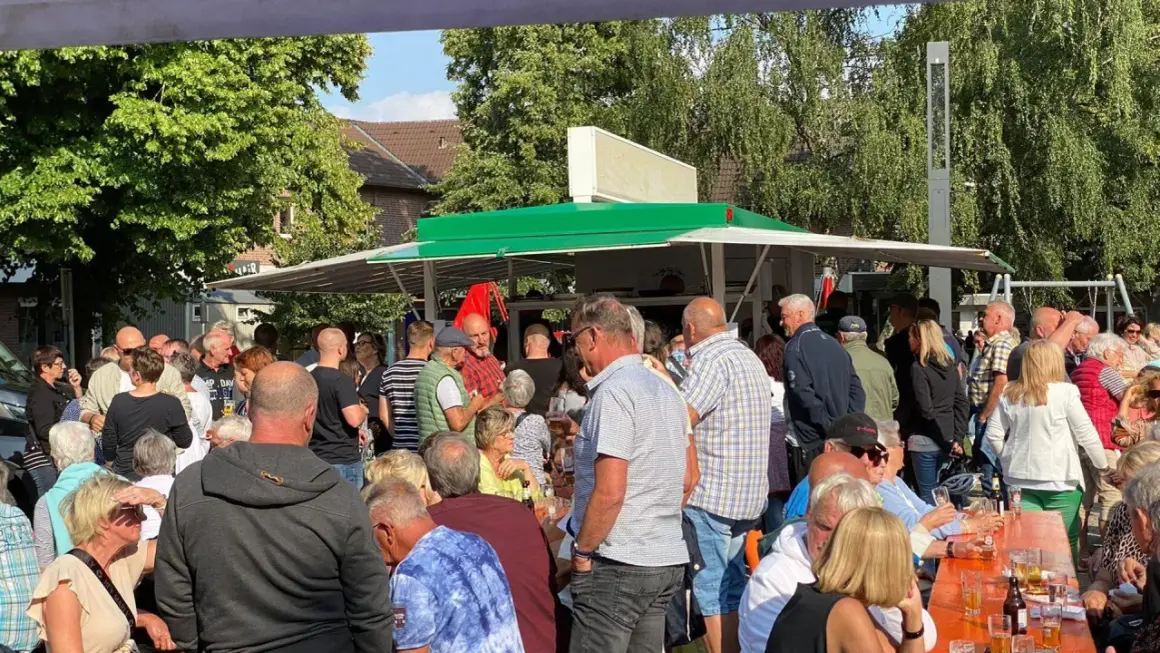 Menschen genießen den feierabendmarkt heute. Viele stehen an einem Imbisswagen, andere sitzen an orangefarbenen Tischen.