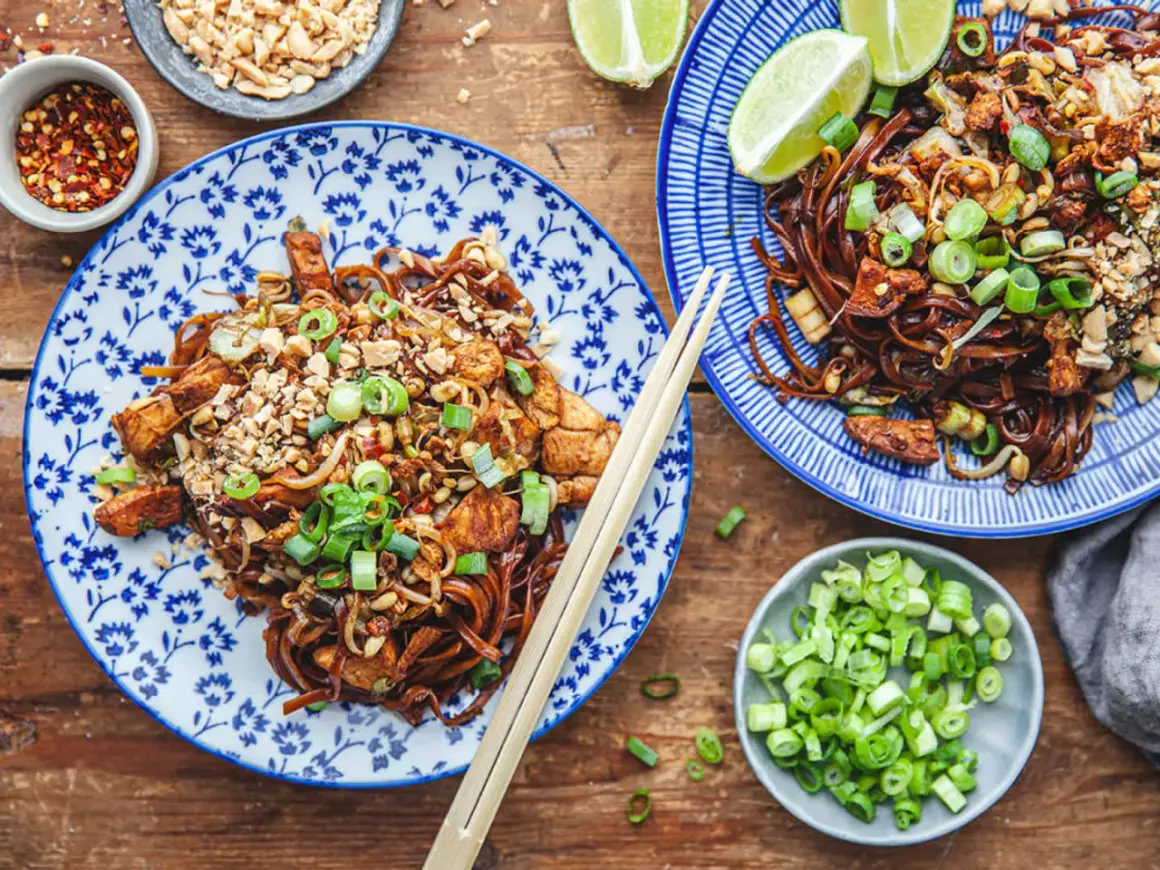 Två tallrikar med läcker pad thai, toppad med jordnötter och salladslök. Ett perfekt pad thai recept för en smakrik måltid.