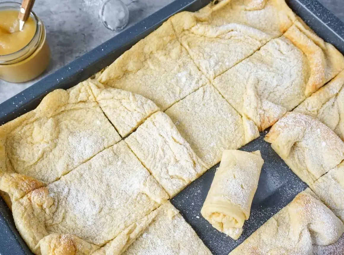 Frisch gebackener Ofenpfannkuchen, in Quadrate geschnitten und mit Puderzucker bestäubt. Ein einzelnes Stück ist aufgerollt und zeigt die Füllung.