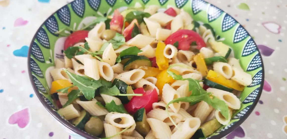 Un piatto colorato di pasta con verdure fresche: zucchine, pomodori, peperoni e rucola.