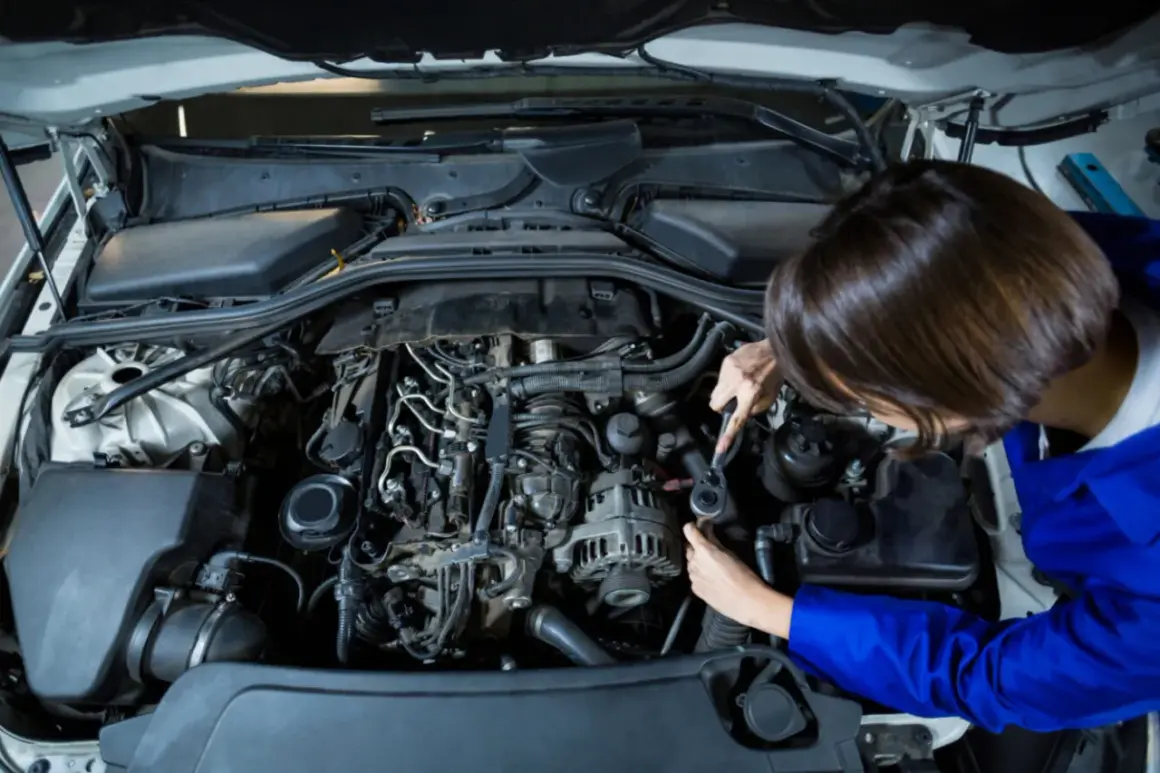 Mechanik naprawia silnik, gdy auto traci moc. Widok z góry na wnętrze komory silnika i ręce trzymające klucz nasadowy.