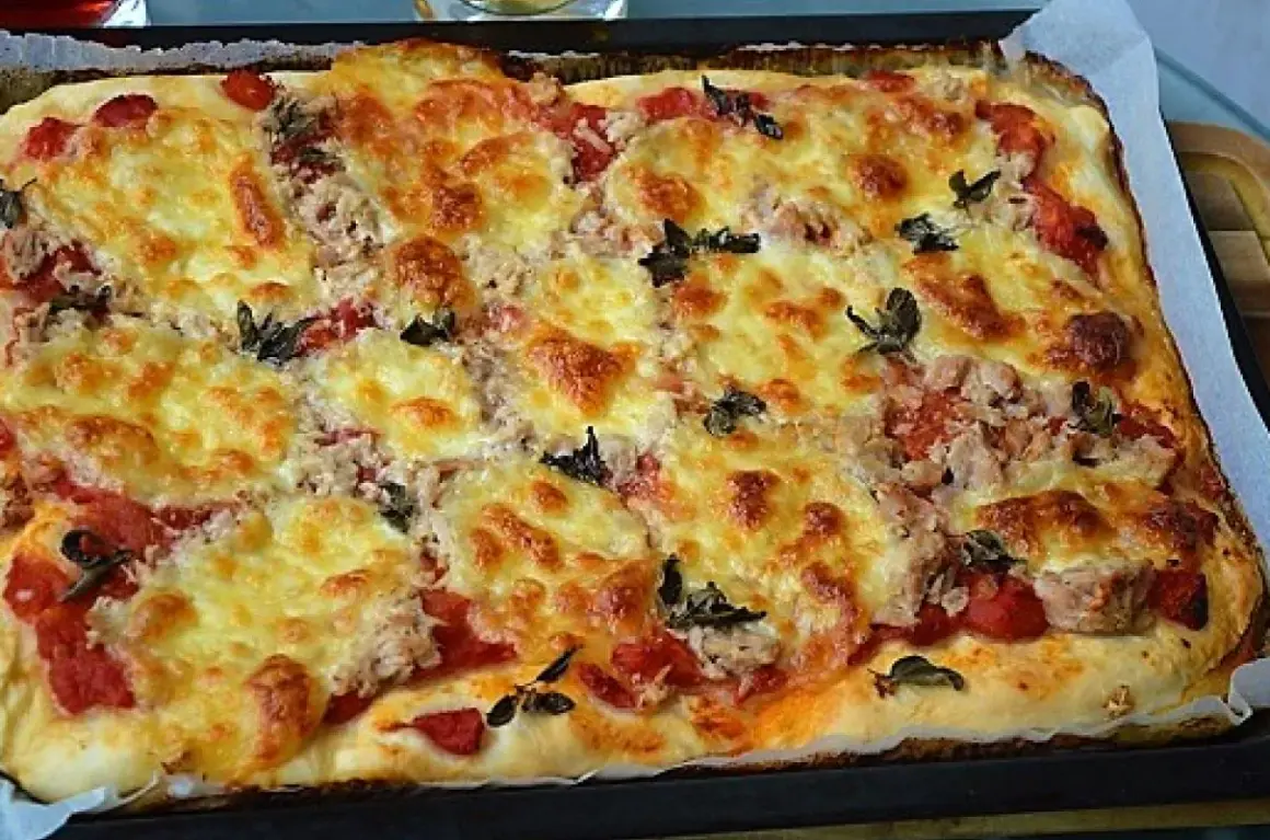 Pyszna, domowa pizza z tuńczykiem, zapieczona pod złotym serem z dodatkiem pomidorów i ziół.