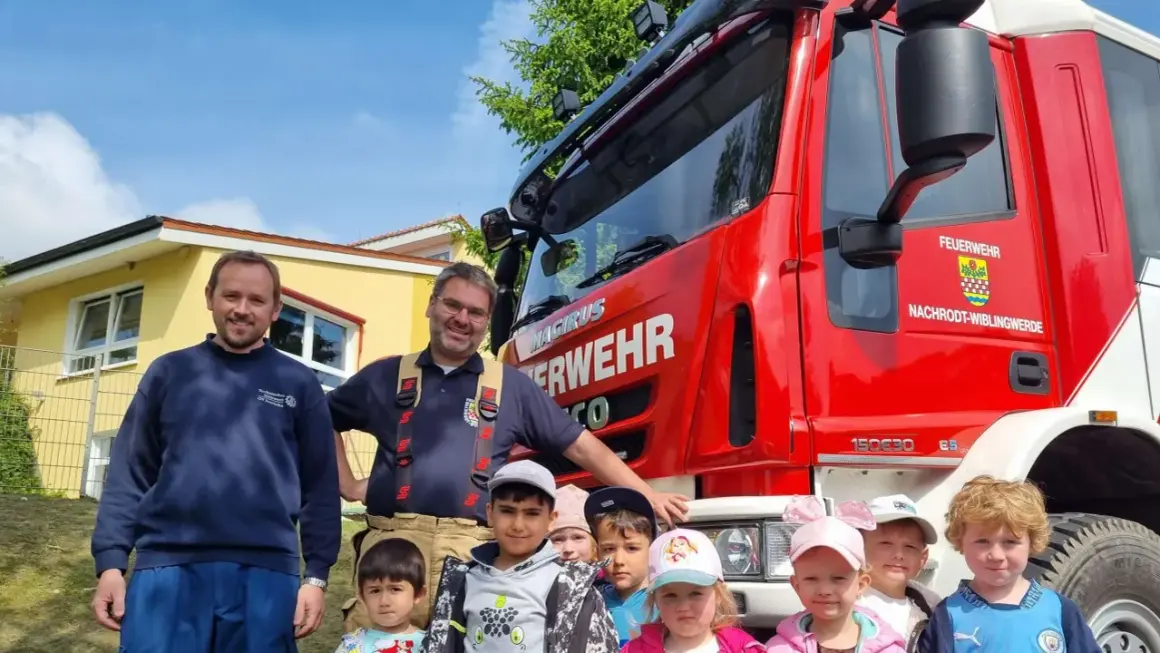 Feuerwehrleute und Kinder vor einem roten Feuerwehrauto. Ein fröhlicher Tag der Feuerwehr!