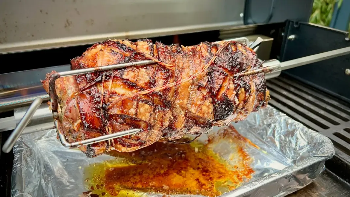 Ein saftiges, am Spieß gebratenes Stück Fleisch, das nach Porchetta aussieht, tropft in eine Aluschale.