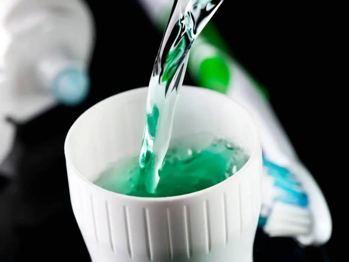 Enjuague bucal verde vertiéndose en un vaso blanco, parte de la rutina de fluorización dental en adultos.