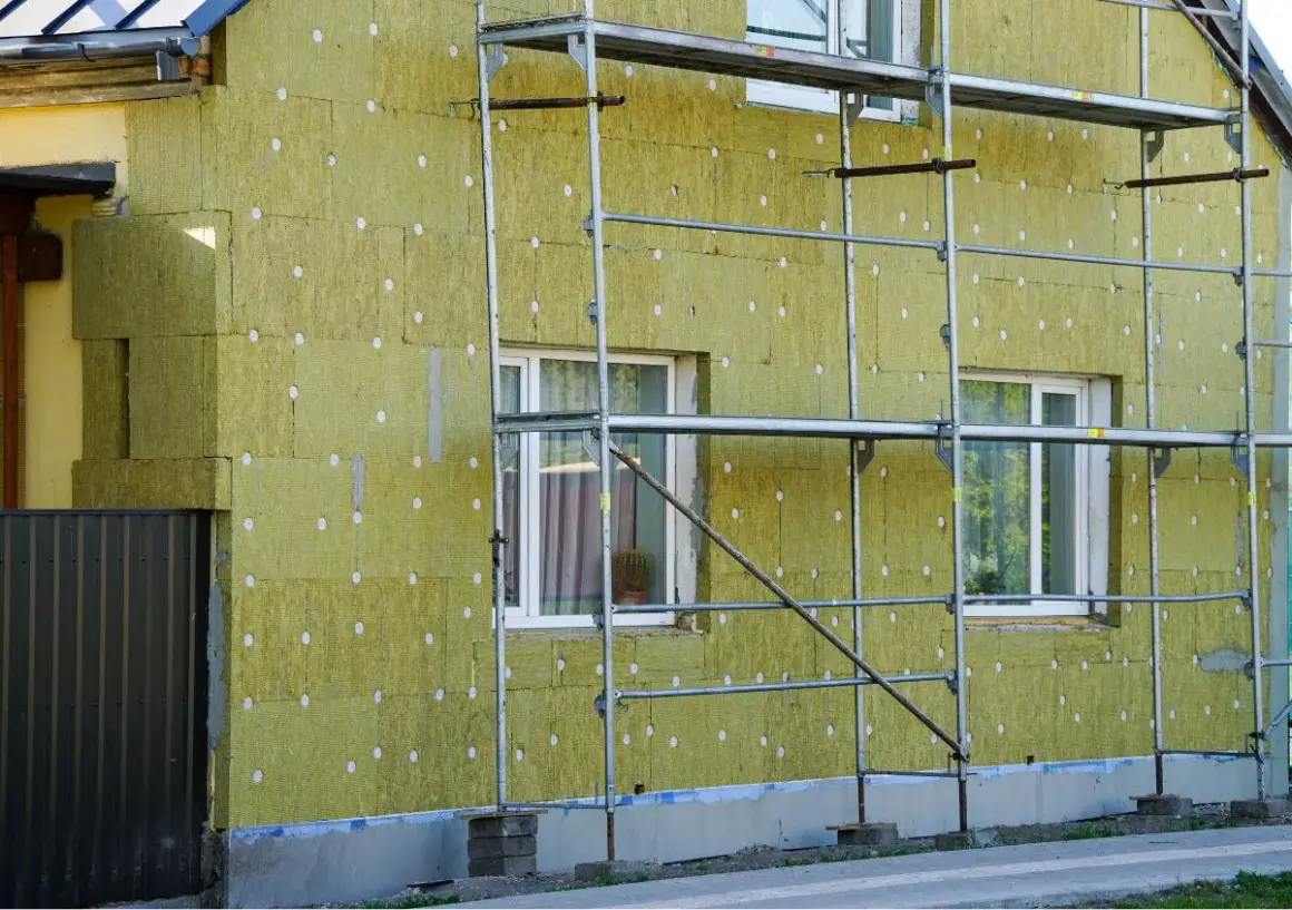 Lavori in corso per pulire muro esterno con cappotto isolante. L'edificio è circondato da ponteggi metallici.