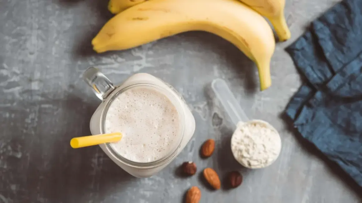 Ein cremiger Proteinshake mit Banane und Nüssen, daneben eine Schaufel Proteinpulver, bereit für das Training. Kreatin im Proteinshake für mehr Power.