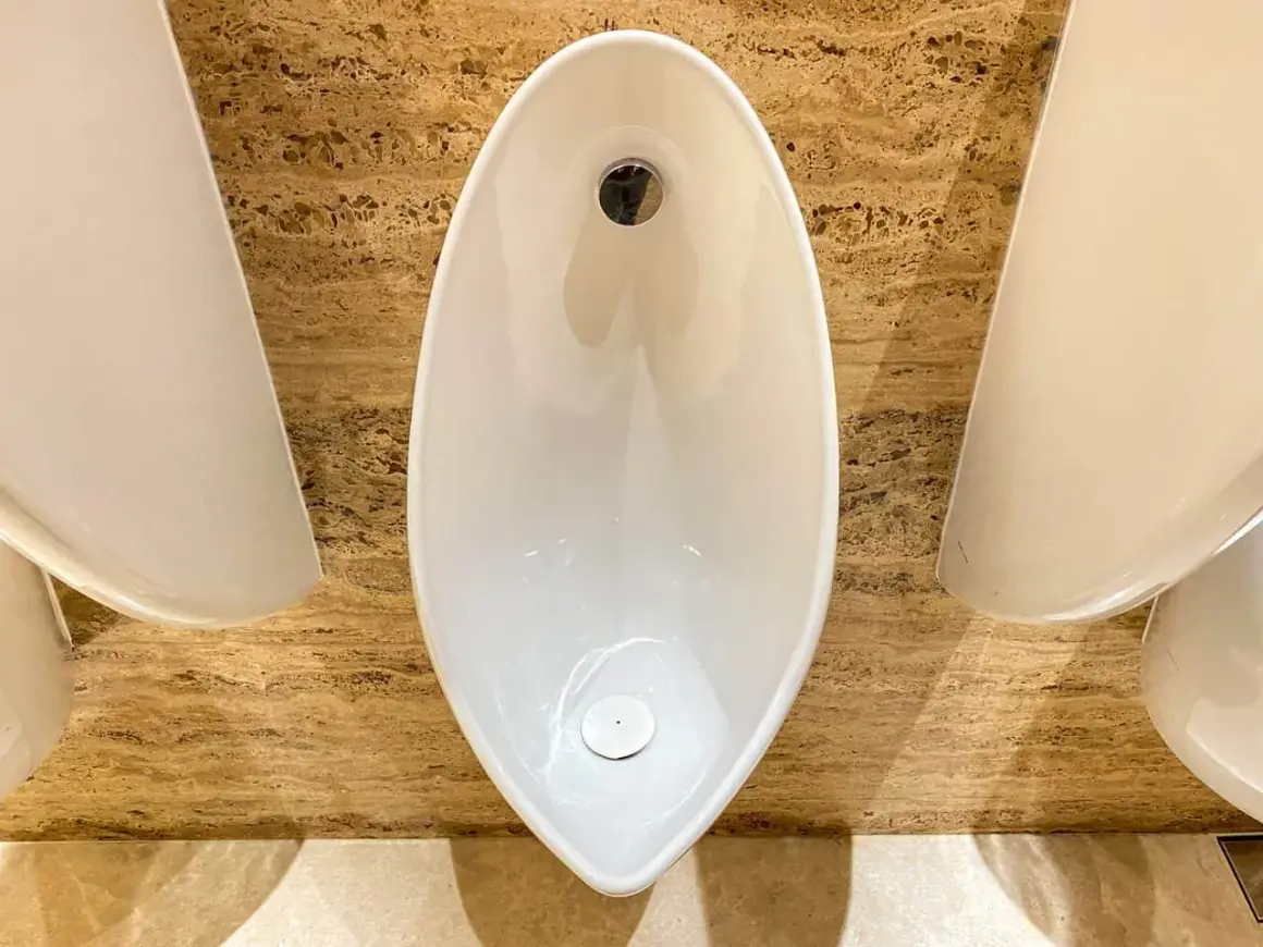 Nowoczesne pisuary o nietypowym kształcie, zamontowane na marmurowej ścianie. Ich wysokość podejść jest ergonomiczna.