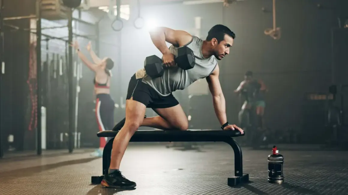 Mann mit shredded body trainiert im Fitnessstudio mit Hanteln.