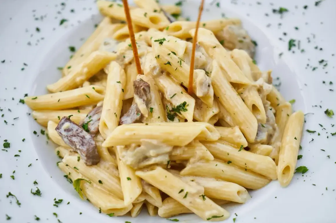 Penne w kremowym sosie z kawałkami mięsa i posypane natką pietruszki.