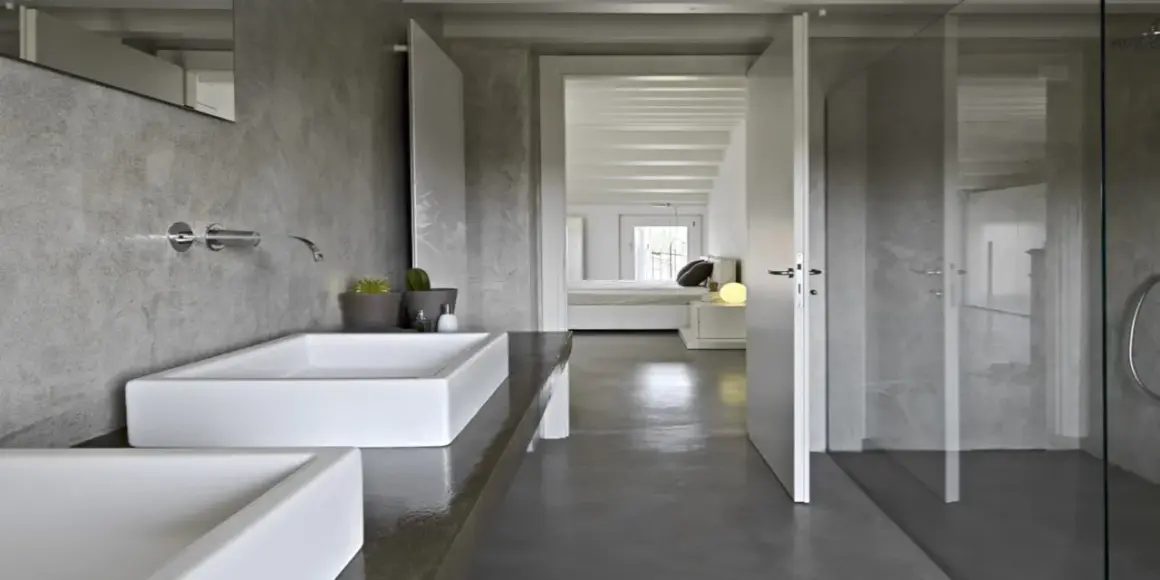 Salle de bain moderne avec murs en béton ciré, lavabos rectangulaires blancs et douche vitrée. La résine salle de bain offre un aspect brut et contemporain.