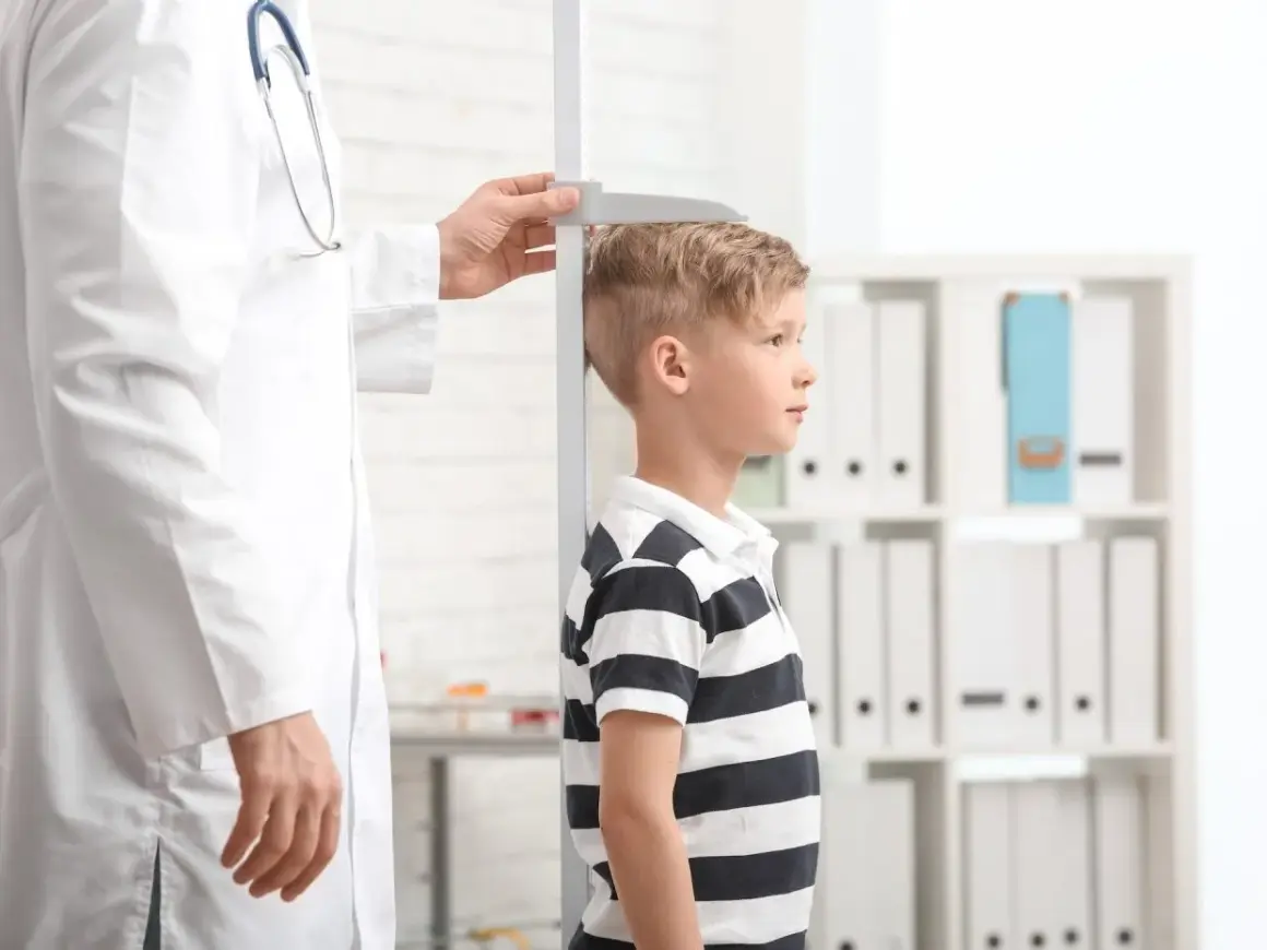 Un bambino viene misurato da un medico. La domanda "quanto sarà alto mio figlio" aleggia nell'aria mentre si attende il risultato.