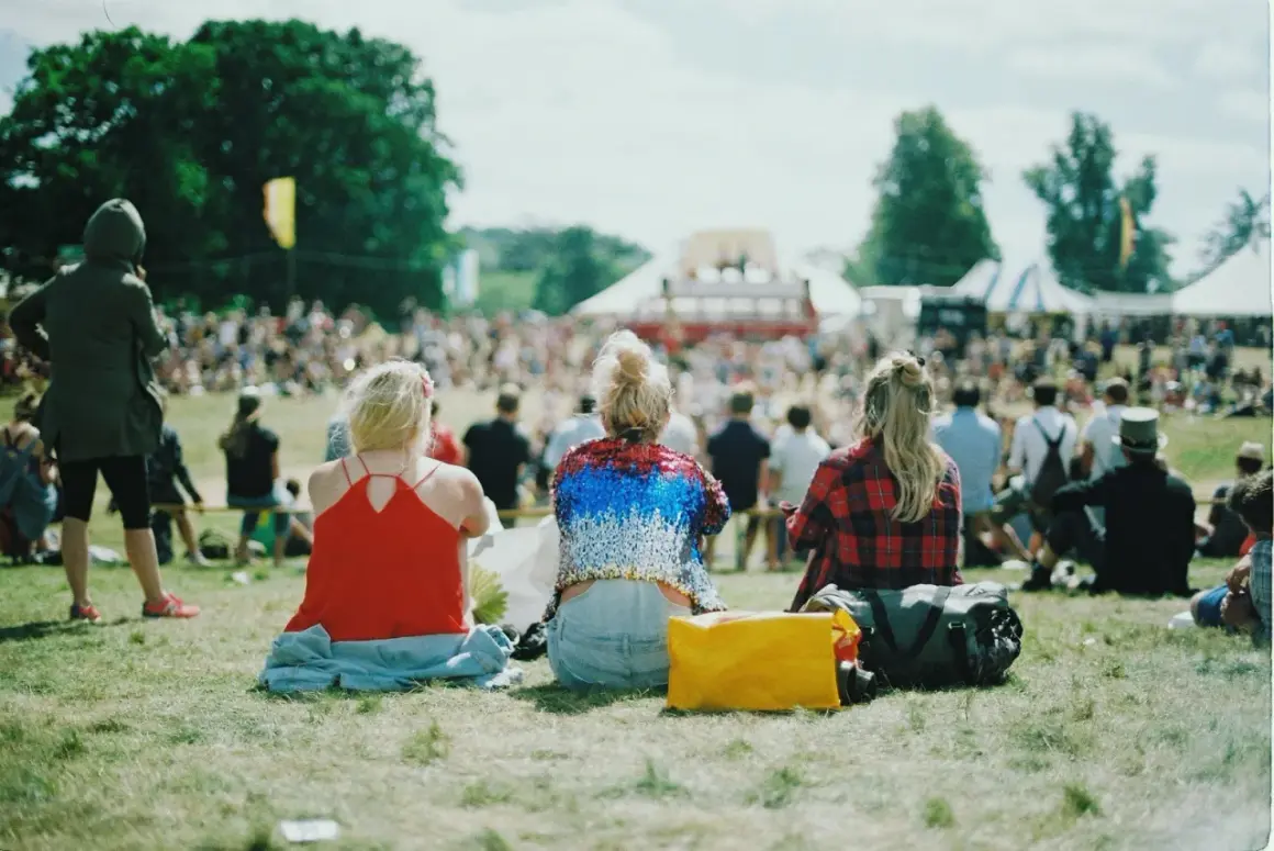 Festivalgäster sitter på gräset med en packlista i åtanke. En gul väska och en stor bag ligger redo för äventyr.