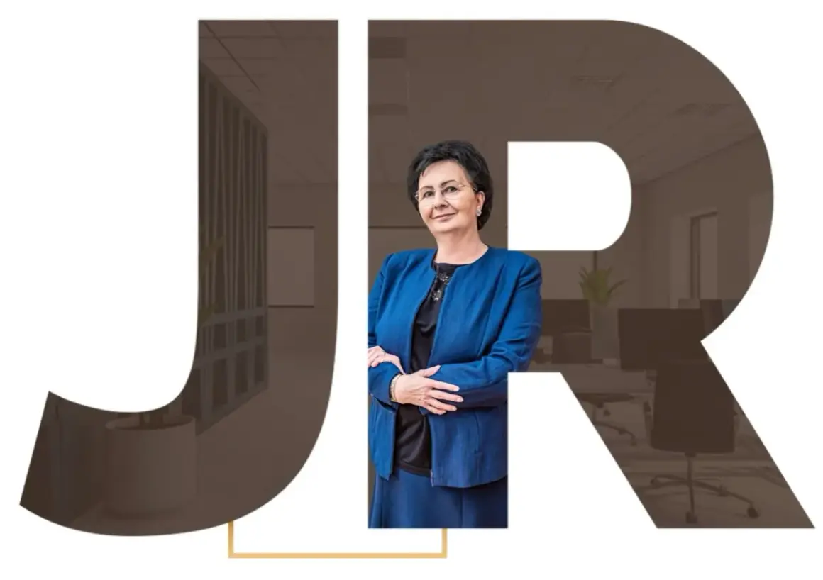 Kobieta w niebieskiej marynarce na tle liter JR i wnętrza biura.