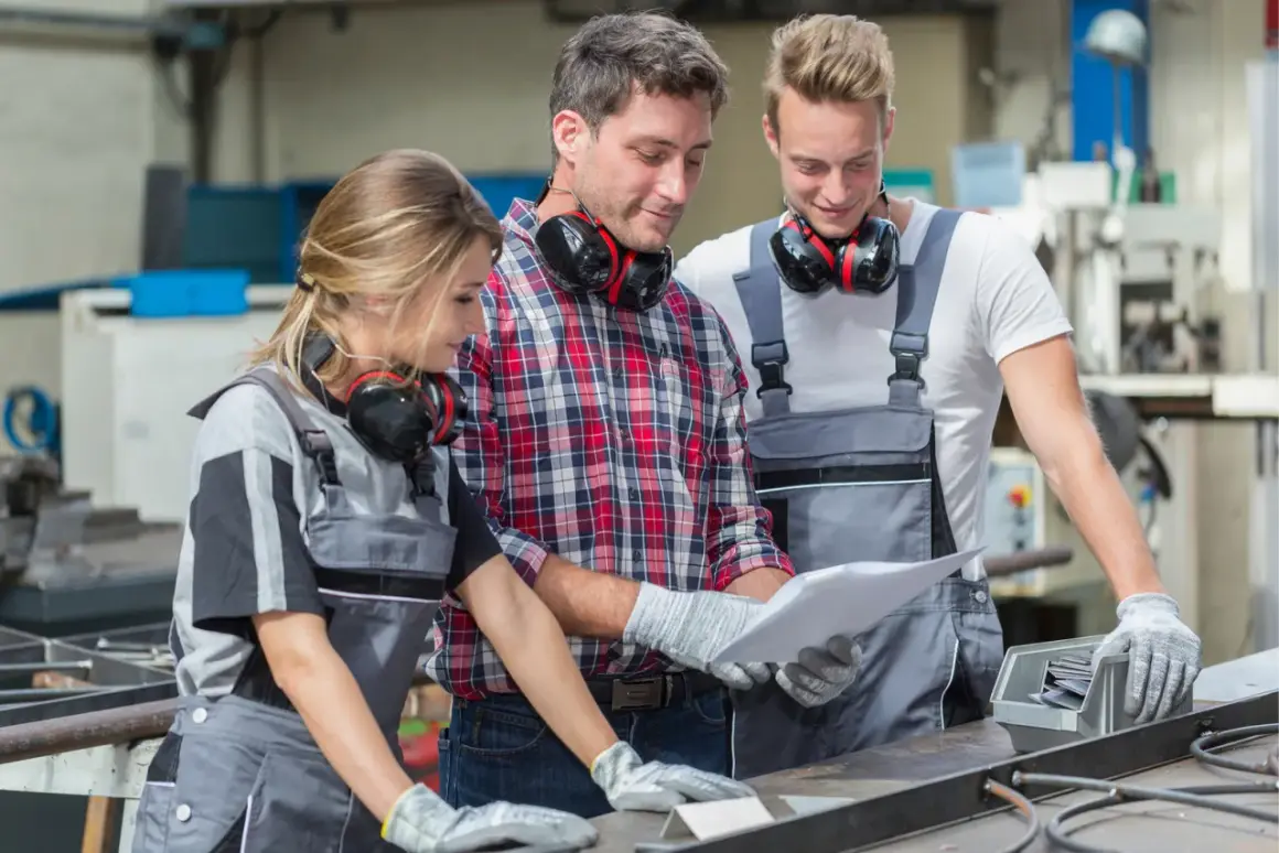 Drei SHK-Techniker besprechen Pläne. Sie tragen Arbeitskleidung und Kopfhörer. Das Gehalt eines SHK-Technikers ist ein wichtiges Thema.