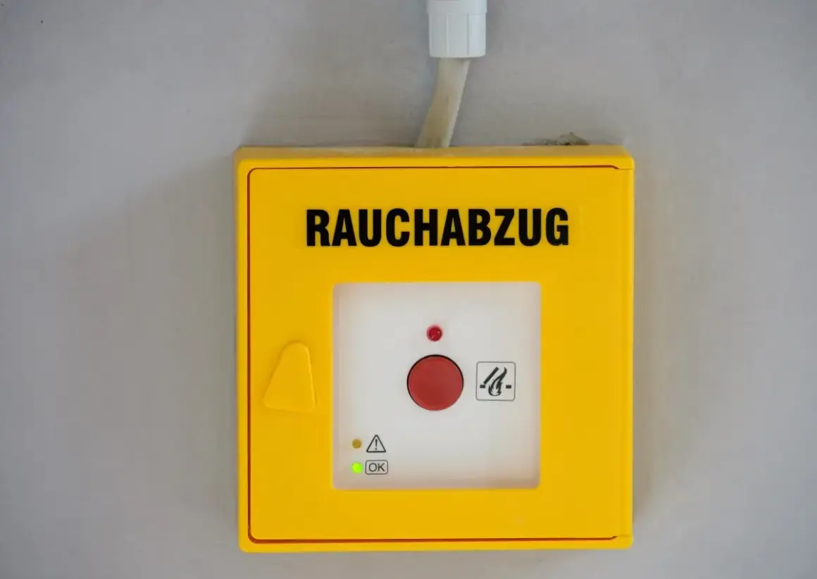 Gelbes Gehäuse für Rauchabzug mit rotem Knopf. Ein grünes Licht zeigt "OK" an, was auf ein erfolgreiches Wartungsprotokoll RWA Muster hindeutet.