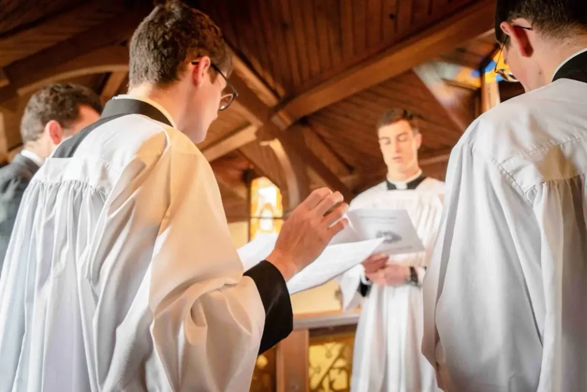 Jeunes hommes en surplis, se préparant pour un baptême protestant. L'un lit un texte, l'autre écoute attentivement.