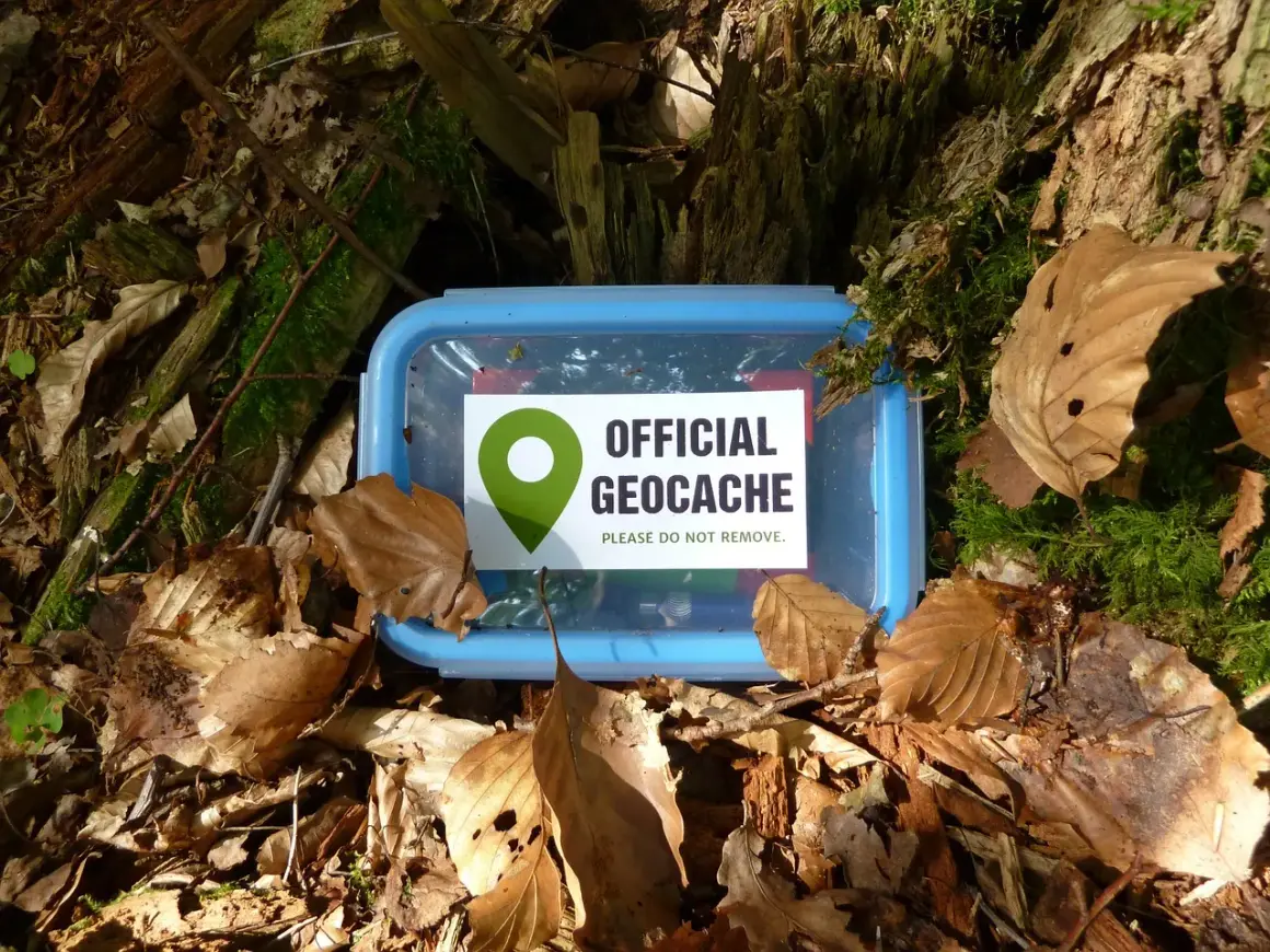 Ein blauer Geocache-Behälter liegt im Wald bei gc Georghausen, bedeckt mit Laub und Moos.