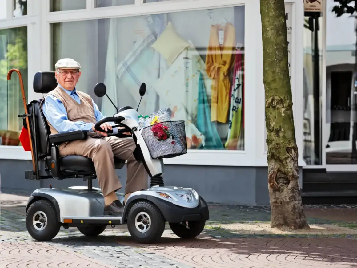 Älterer Herr im elektrischen Rollstuhl vor einem Schaufenster. Dank der Krankenkasse kann er mobil bleiben.