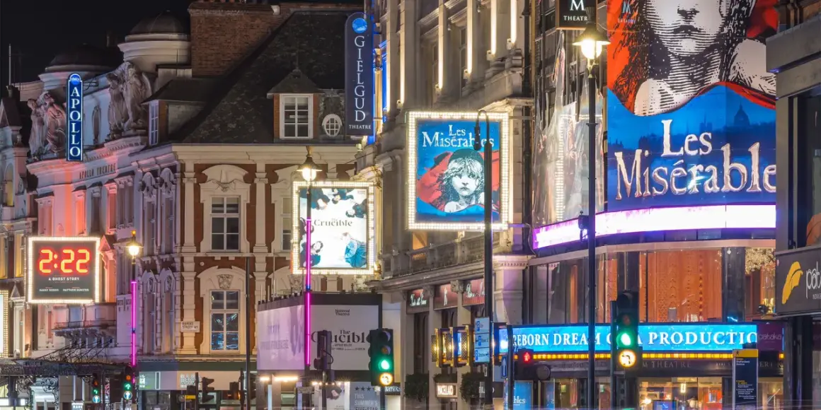 Nocne światła teatrów w londyńskim **West Endzie**: plakaty "Les Misérables", "The Crucible" i "2:22 A Ghost Story" oświetlają ulicę.
