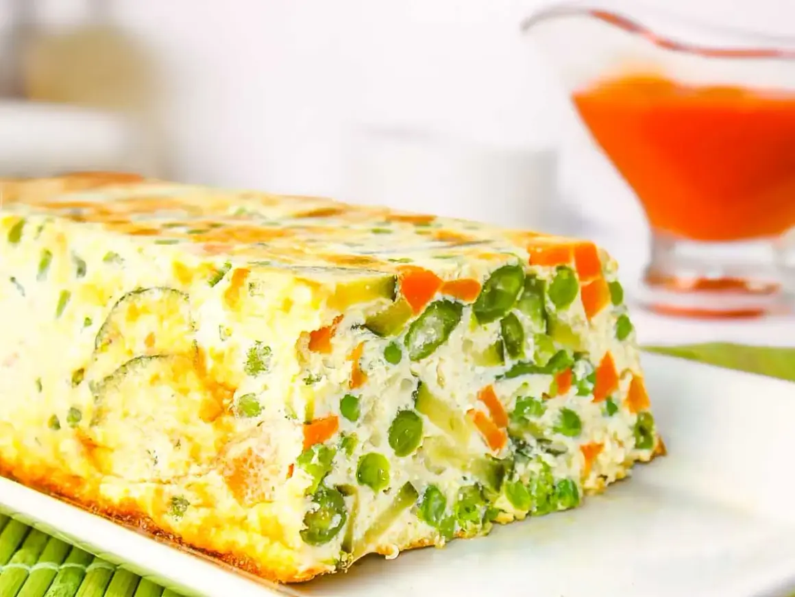 Un delicioso pastel de verduras, con guisantes, zanahoria y calabacín, horneado en un molde rectangular.
