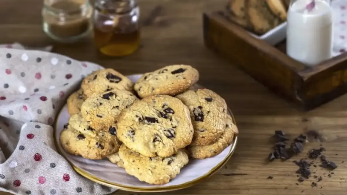 Montón de galletas con pepitas de chocolate recién horneadas, listas para disfrutar con un vaso de leche.