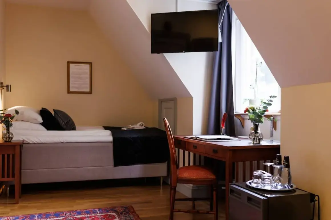 A hotel room with a bed, desk, chair, and a TV mounted on the wall.