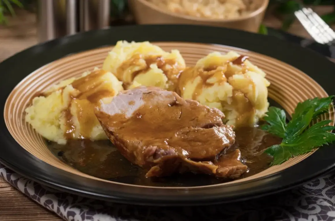 Pyszna karkówka w sosie podana z purée ziemniaczanym i gałązką natki pietruszki.