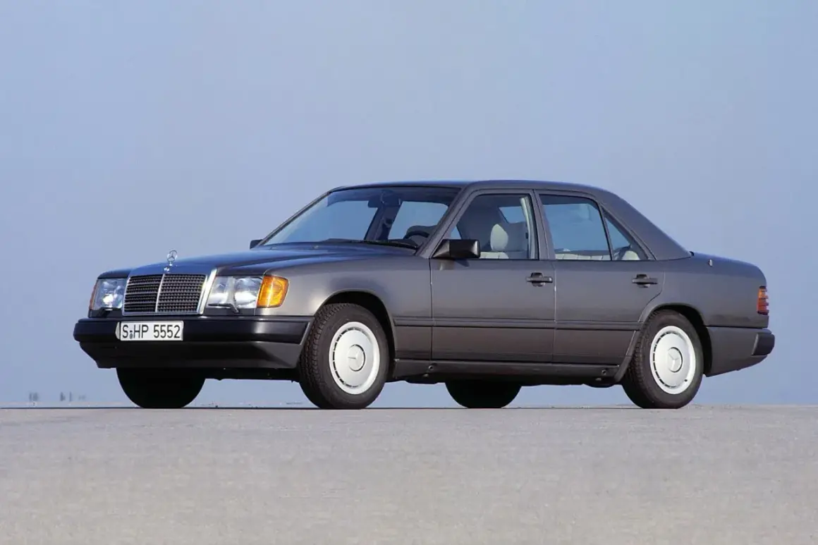 Szary Mercedes-Benz W124, symbol najbardziej niezawodnych samochodów, stoi na pustej drodze.