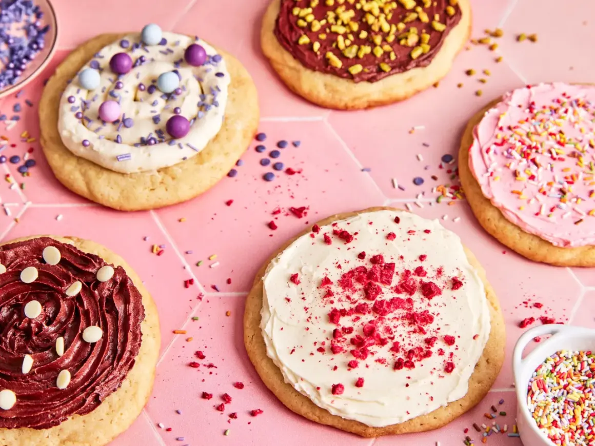 Bunte, verzierte Kekse, darunter ein mit weißer Creme und roten Krümeln bestreuter **crumble cookie**.