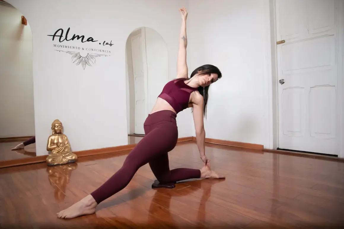 Mujer en postura de yoga, demostrando la fluidez del vinyasa yoga. Reflejo en espejo y Buda dorado.