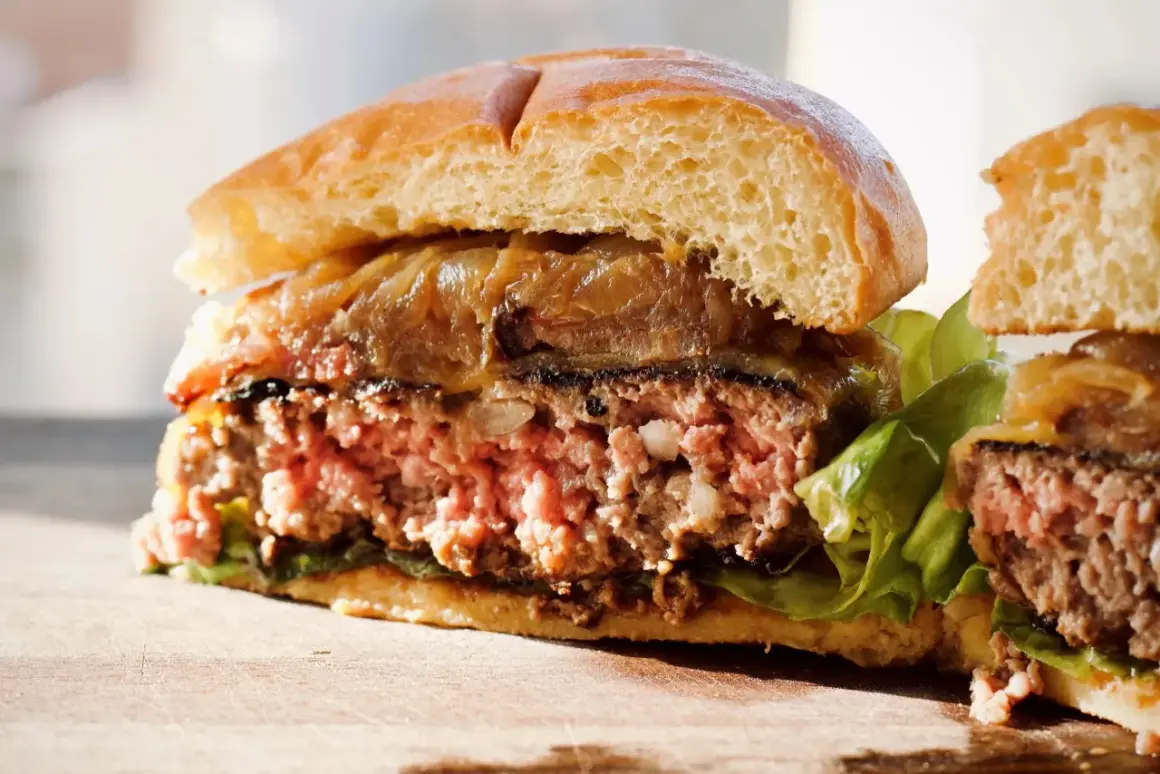Przekrojony, soczysty burger z karmelizowaną cebulą i sałatą na desce.