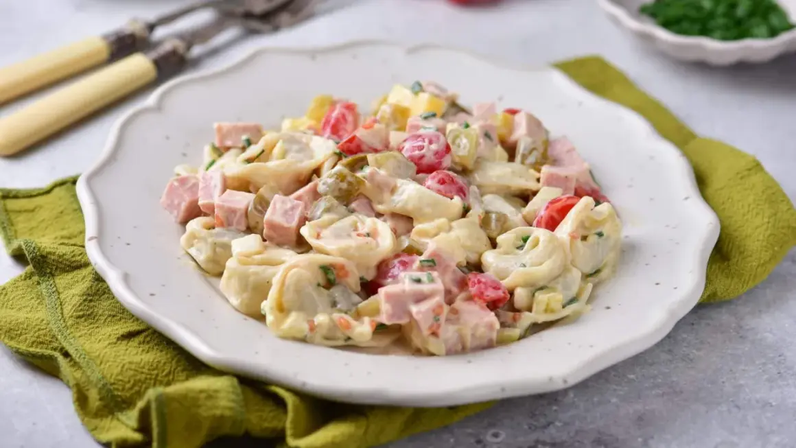 Prosta sałatka z tortellini, szynką, pomidorkami i ogórkiem konserwowym, polana kremowym sosem.