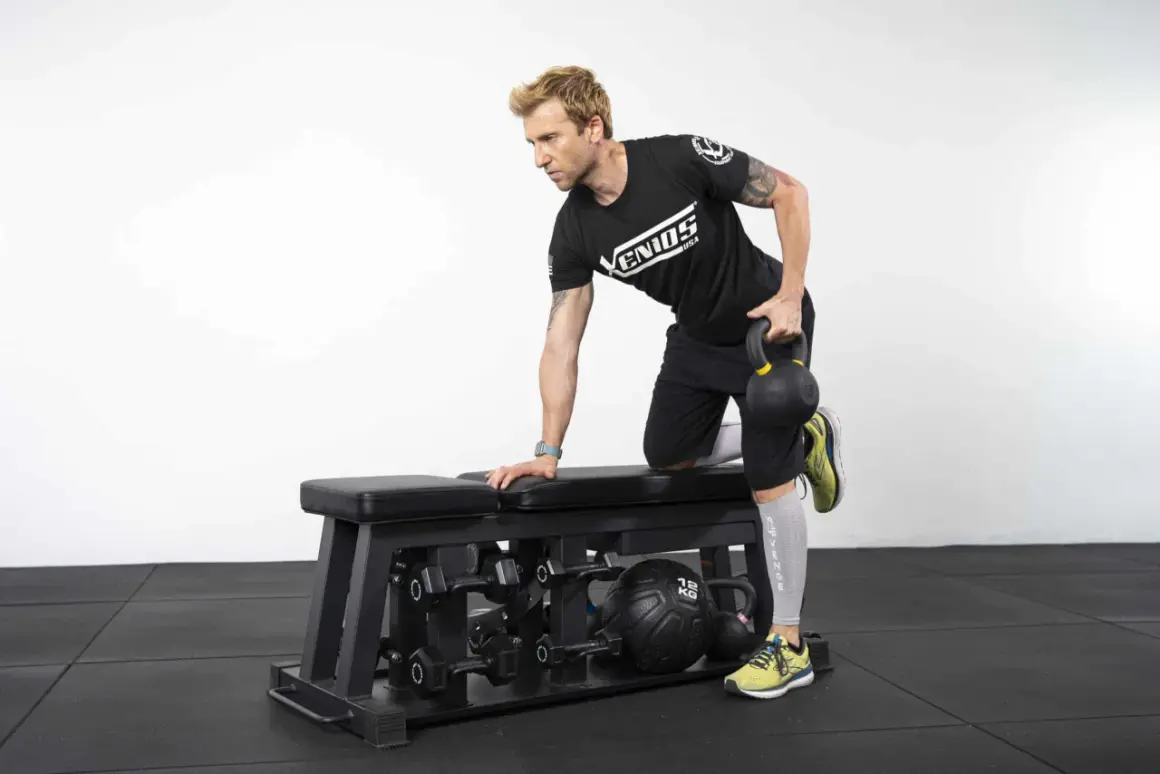 Homme effectuant un exercice de tirage avec kettlebell sur un banc de musculation.