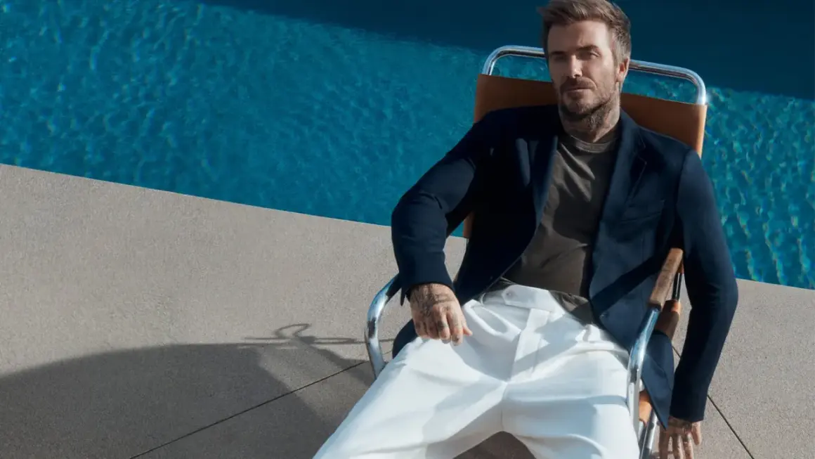 David Beckham style: en man i mörk kavaj och vita byxor sitter vid en pool.