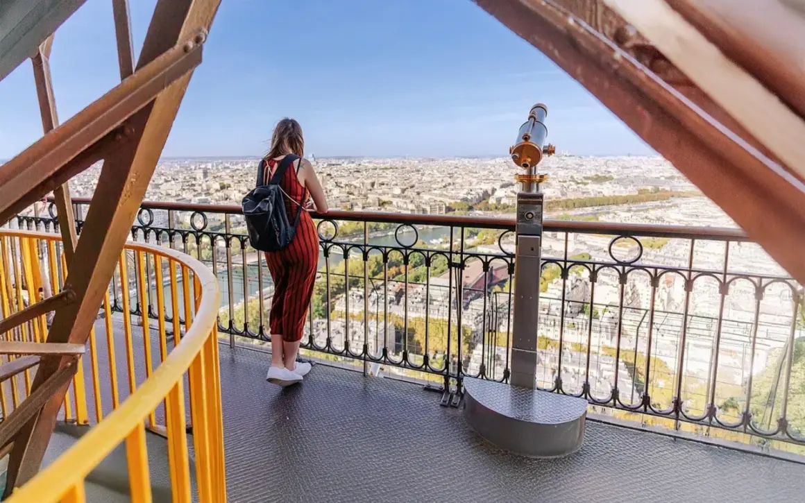 En kvinna med ryggsäck njuter av utsikten över Paris från Eiffeltornet. Hon undrar nog hur många trappsteg har Eiffeltornet.