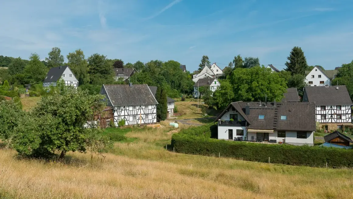 Fachwerkhäuser säumen den malerischen fachwerkweg Ruppichteroth, eingebettet in grüne Hügel unter blauem Himmel.