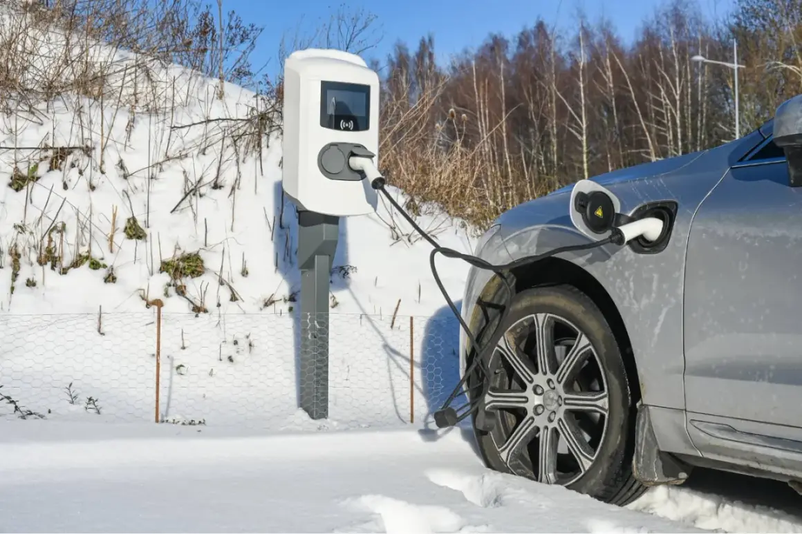 Une voiture électrique grise est branchée à une borne de recharge dans un paysage enneigé. Le chauffage de la voiture électrique est assuré par cette connexion.