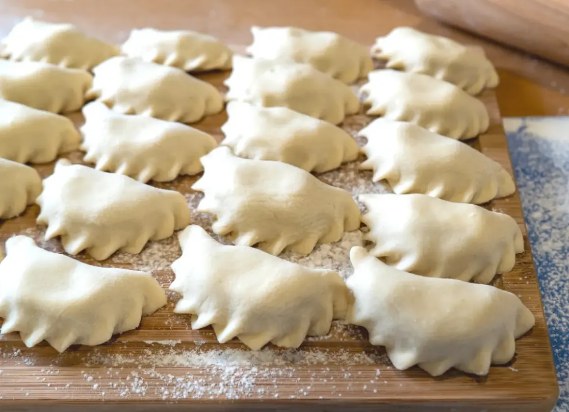 Rządki surowego ciasta na pierogi ułożone na desce, posypanej mąką.