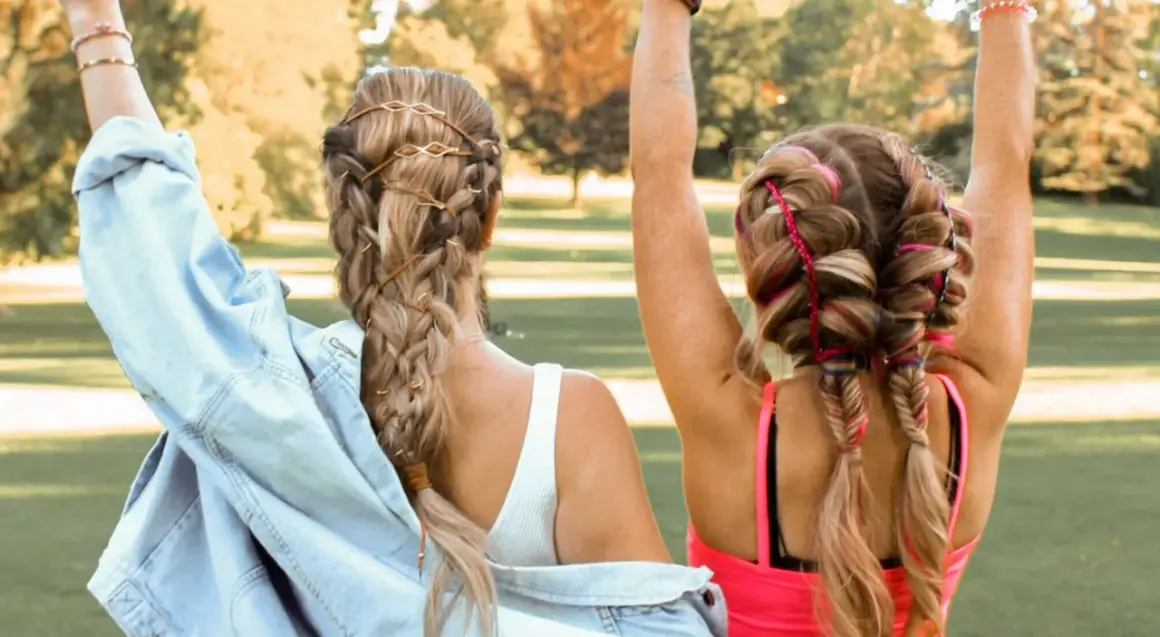Zwei Mädchen mit geflochtenen Haaren, die sich für festival frisuren einfach eignen. Eine trägt braune Bänder, die andere bunte Fäden.