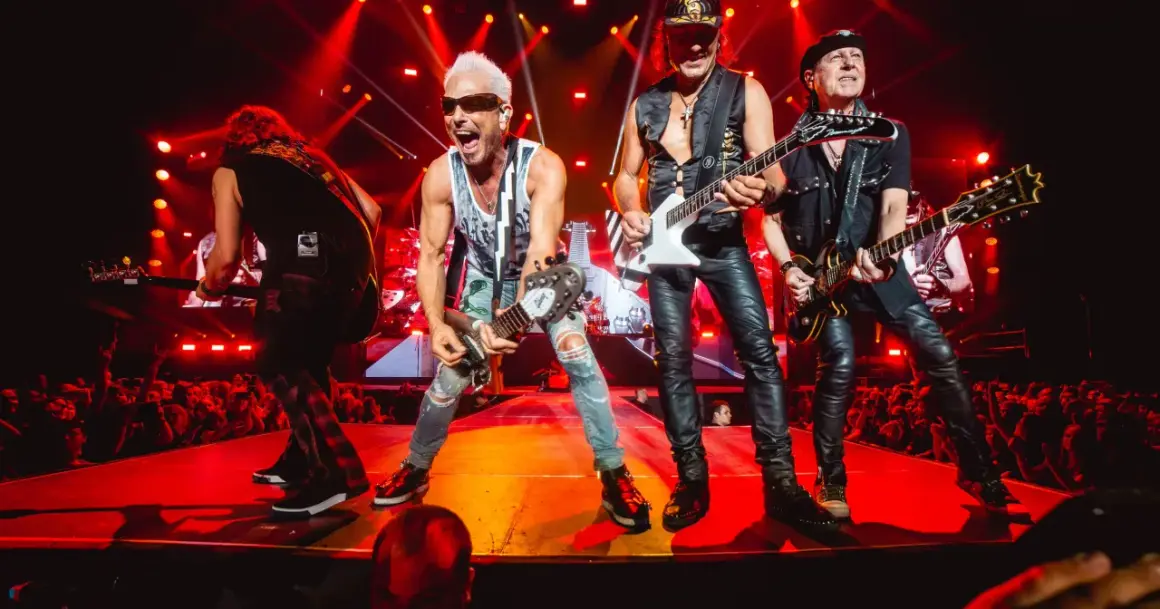 Zespół Scorpions na koncercie, grający swoje rockowe ballady. Wokalista z blond włosami i w okularach krzyczy do mikrofonu.